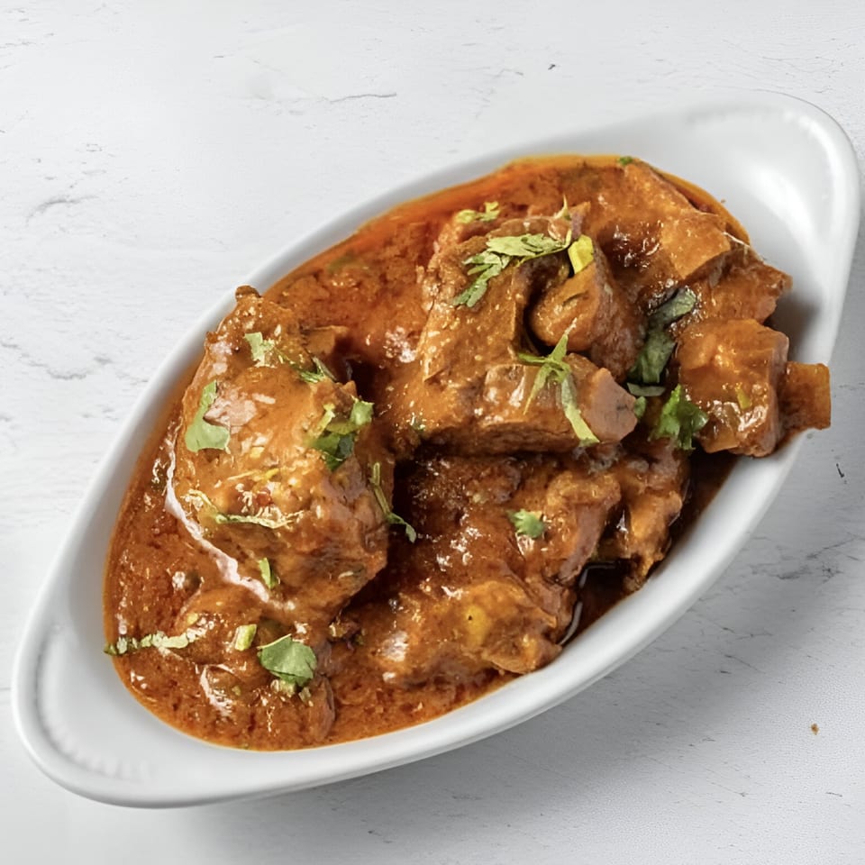 Taj Darbar Indian Cuisine's chicken curry, a rich brown stew with green herb garnish in a white dish.