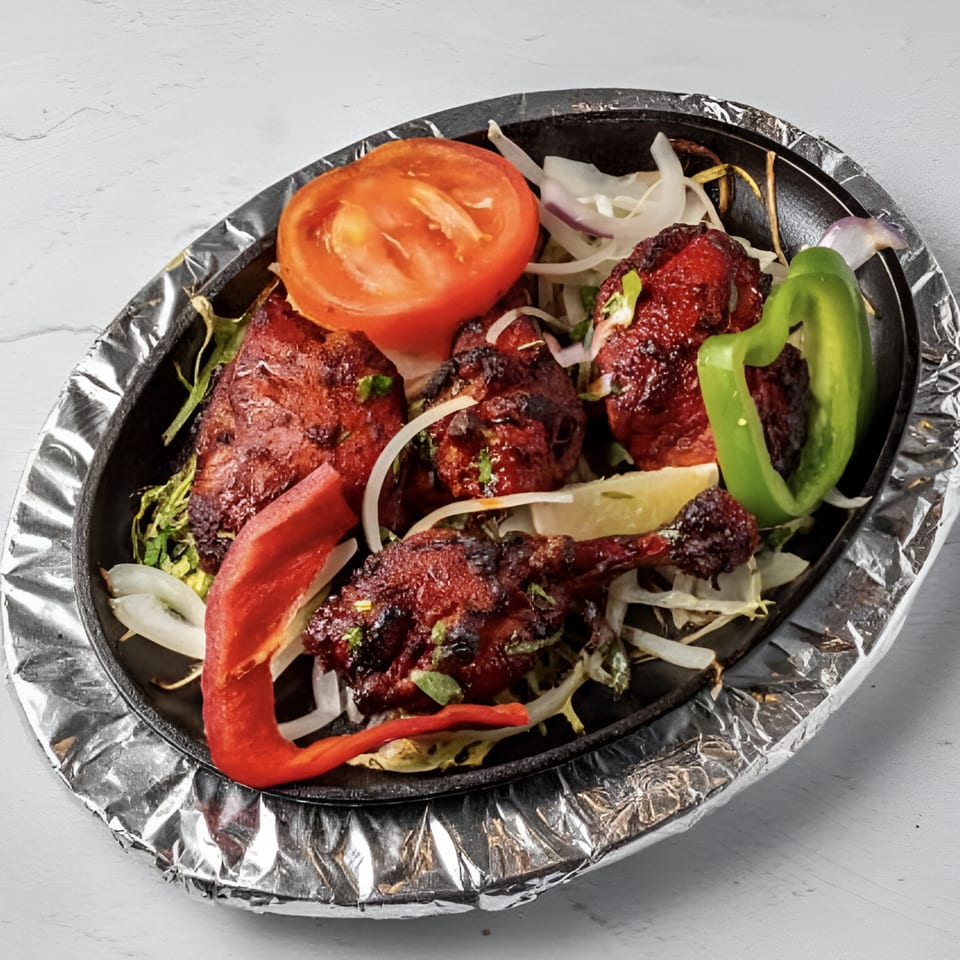 Taj Darbar Indian Cuisine's chicken tikka sizzler with onions, peppers, and tomato on a foil-lined platter.