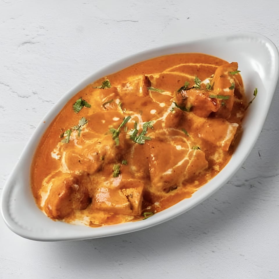 Taj Darbar Indian Cuisine's creamy orange curry with paneer and cilantro in a white dish.